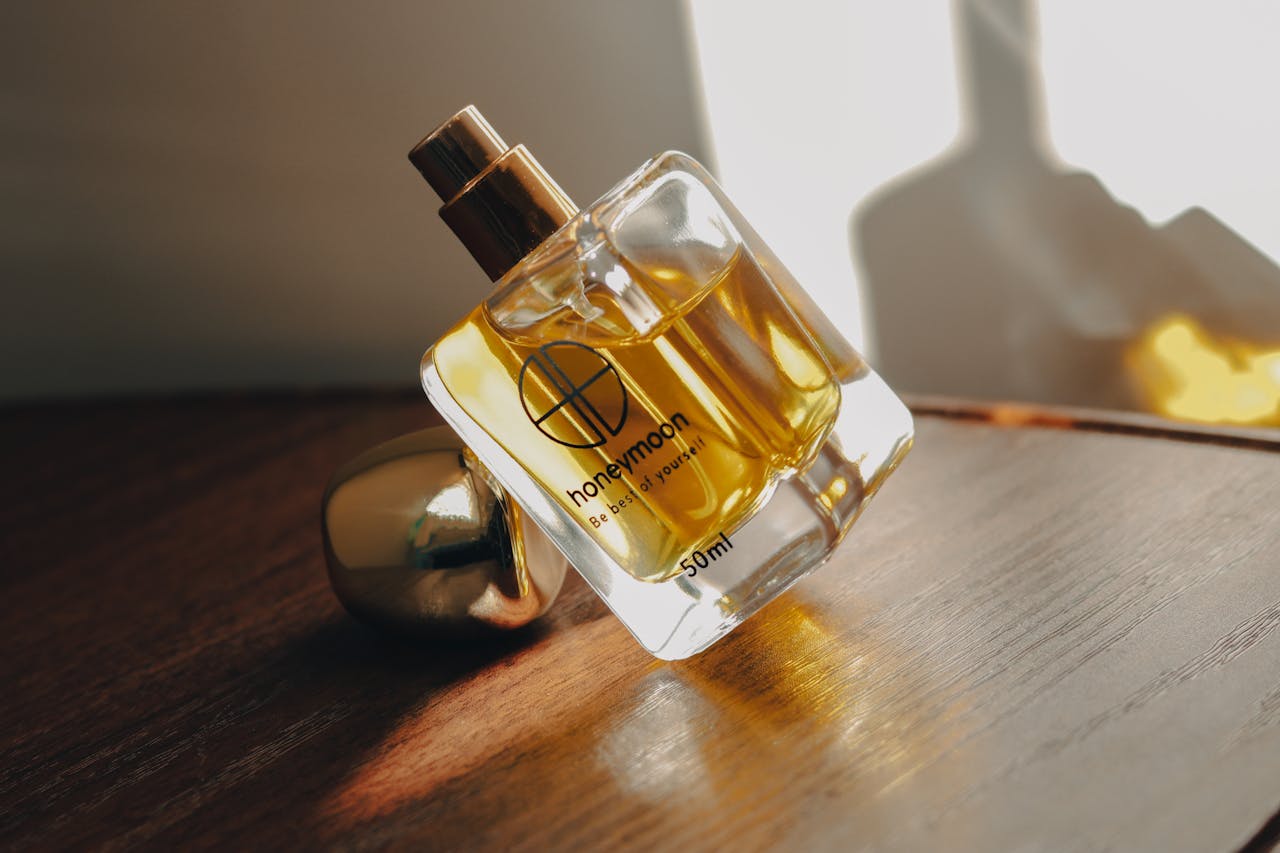 menu-02 A clear glass perfume bottle with golden liquid on a wooden surface, softly lit.